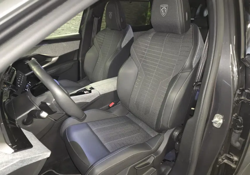 Vue intérieure côté conducteur du Peugeot 5008 gris 2025, sièges tissu et cuir avec logo Peugeot brodé sur appuie-tête.
