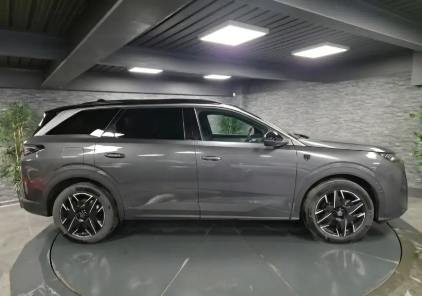 Vue de profil côté gauche d'un Peugeot 5008 gris métallisé 2025 en hybride essence, avec jantes alliage noires et toit noir.