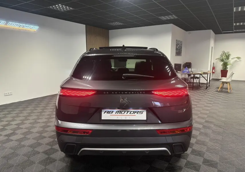 Vue arrière d'un DS7 Crossback gris métallisé avec feux arrière LED 3D allumés dans un showroom.