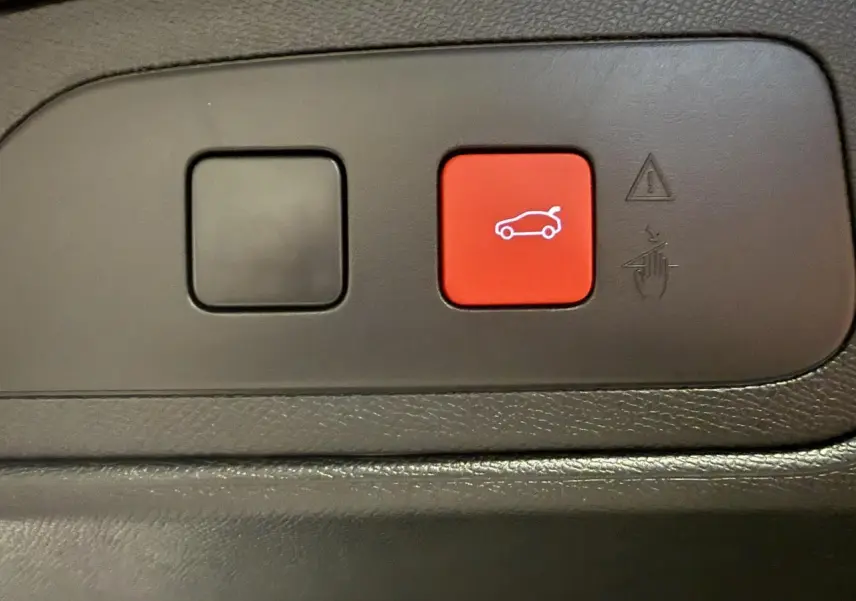 Gros plan sur le bouton rouge d'ouverture du hayon dans l'habitacle du DS7 Crossback gris 2025.