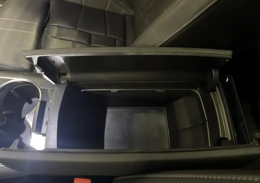 Vue rapprochée de la console centrale ouverte avec rangement intérieur noir du DS7 Crossback gris, sièges en cuir visibles.