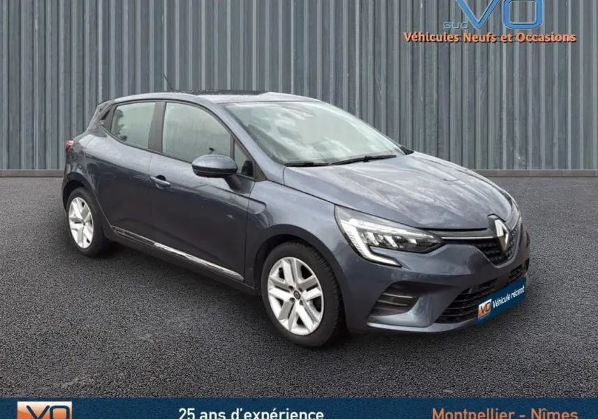 Renault Clio V Blue dCi 85 Business gris foncé vue 3/4 avant droit sur sol noir devant un mur métallique.