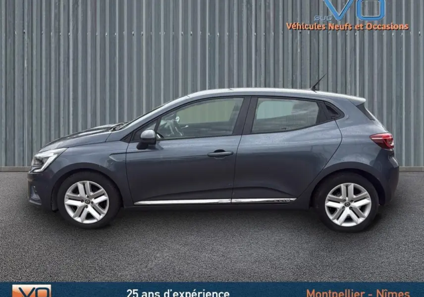 Profil côté gauche d'une Renault Clio V Blue dCi 85 Business gris foncé, vue extérieure sur fond industriel.