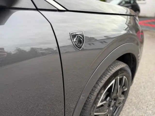 Gros plan sur l'aile avant droite gris titane du Peugeot 3008 avec logo lion et jante alliage noire.