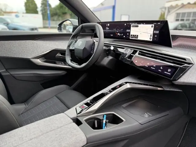 Vue intérieure côté conducteur du Peugeot 3008 Hybrid 145 GT 2025, avec volant cuir multifonction, sellerie tissus gris et écran panoramique incurvé.