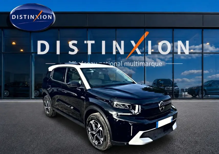 Vue 3/4 avant droite d'un Citroën C3 Aircross noir avec toit blanc et jantes alu devant un showroom Distinxion.