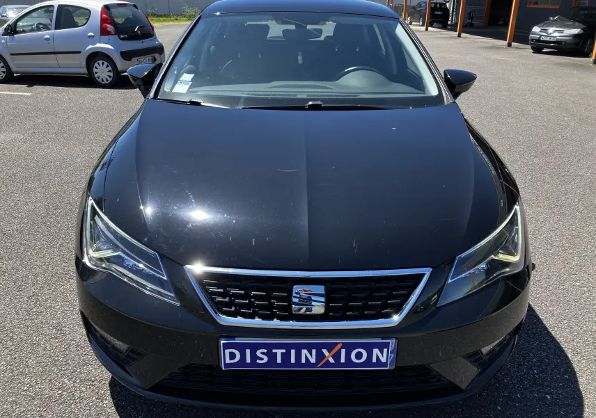 Vue frontale d'une SEAT LEON noire 2018 avec calandre chromée et plaque Distinxion visible sur un parking.