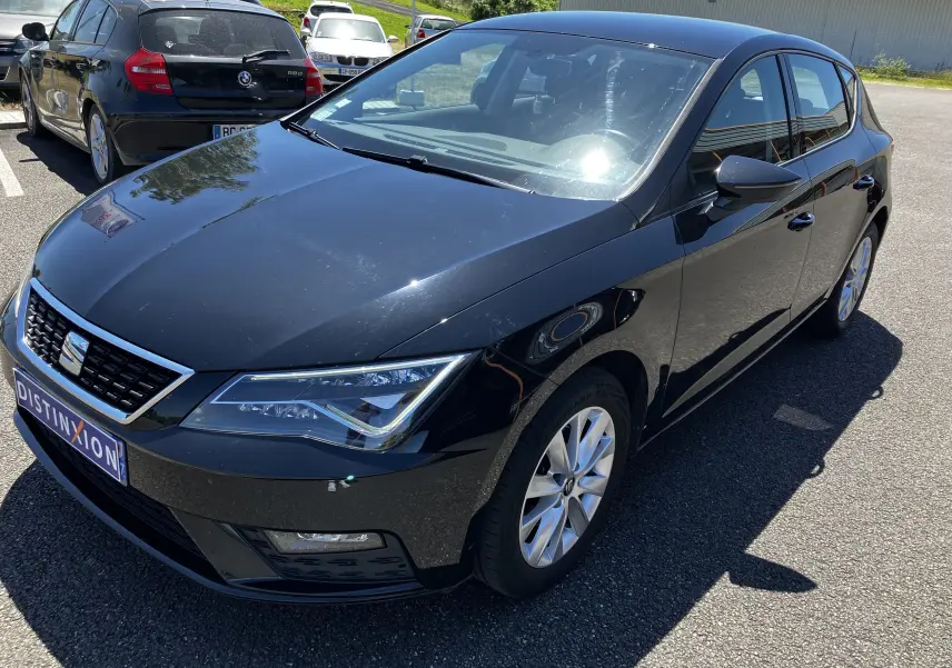 SEAT Leon 1,6L TDI 115 Style noir en 3/4 avant droit, avec jantes alliage et calandre chromée visible.