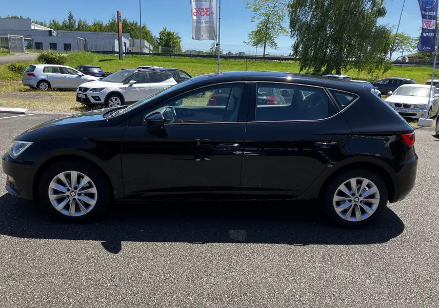 Profil latéral droit d'une SEAT LEON noire 5 portes, garée en extérieur par temps ensoleillé.