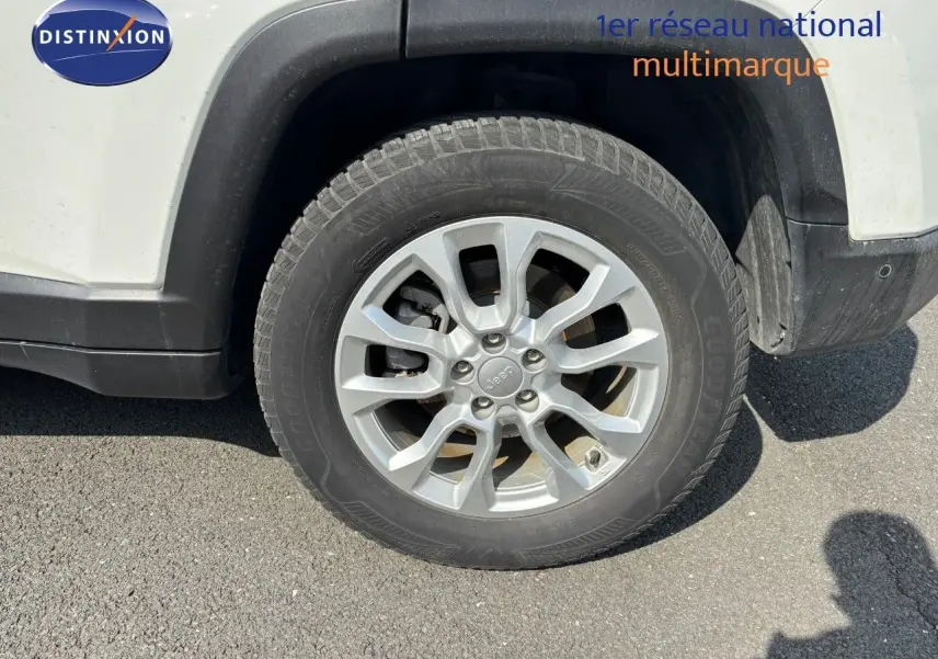 Gros plan sur la roue avant droite d'un Jeep Compass blanc, mettant en valeur la jante alliage et le pneu Goodyear.