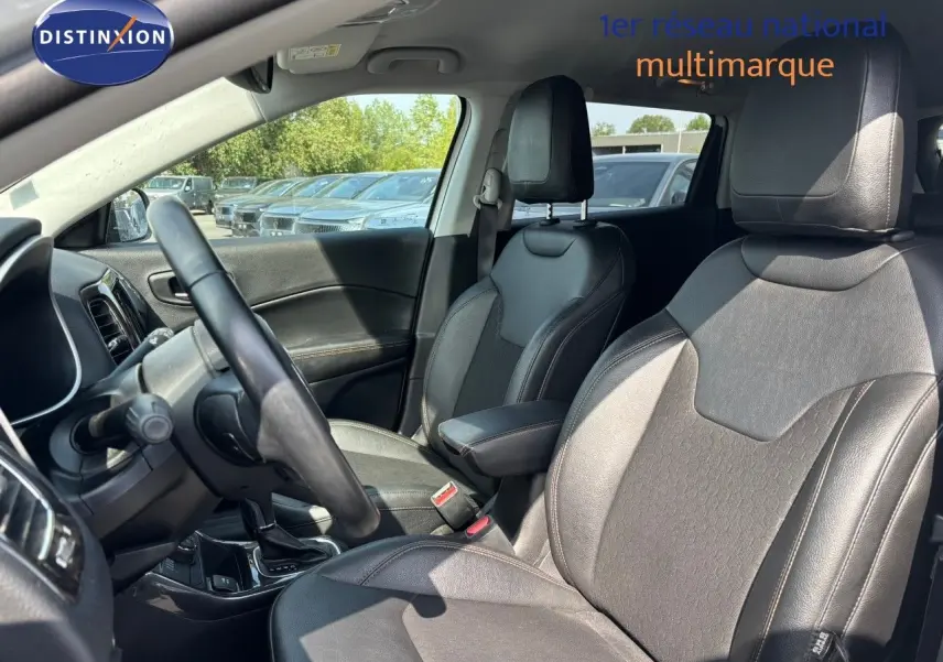 Vue intérieure côté conducteur du Jeep Compass 2021 blanc, sièges en cuir noir avec accoudoir central et tableau de bord visible.