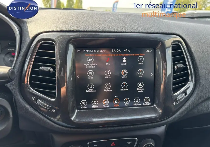 Écran tactile central du tableau de bord du Jeep Compass blanc, affichant les commandes multimédia et climatisation.