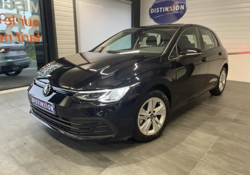 Volkswagen Golf 1.5 eTSI noire vue 3/4 avant en intérieur avec jantes alliage et logo lumineux sur calandre.