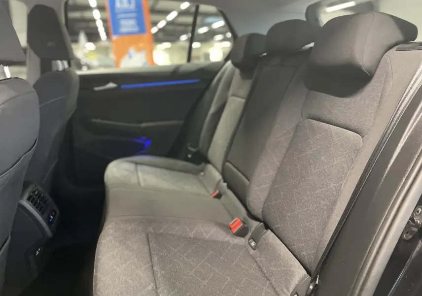 Vue intérieure côté droit des sièges arrière gris foncé de la Volkswagen Golf 1.5 eTSI Style 2024 avec éclairage d'ambiance bleu.