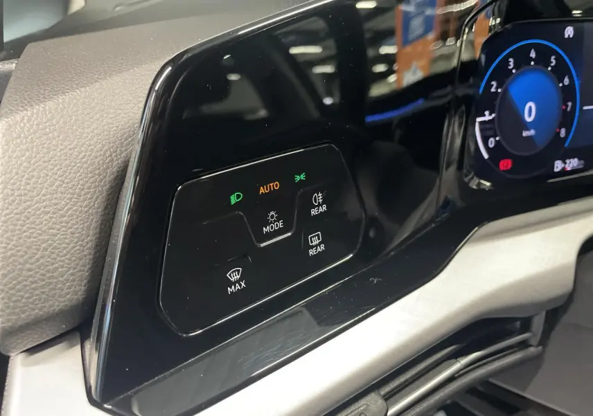 Détail du tableau de bord noir brillant de la Volkswagen Golf 2024 avec commandes d'éclairage et écran digital partiel.