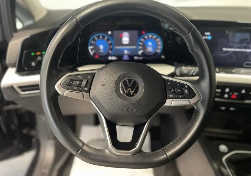 Vue rapprochée du volant noir en cuir de la Volkswagen Golf 1.5 eTSI 2024 avec tableau de bord digital lumineux.