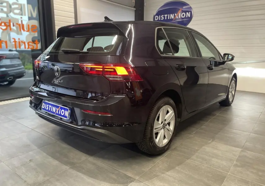 Volkswagen Golf 1.5 eTSI noire vue 3/4 arrière droit en intérieur avec feux arrière allumés et jantes alliage.