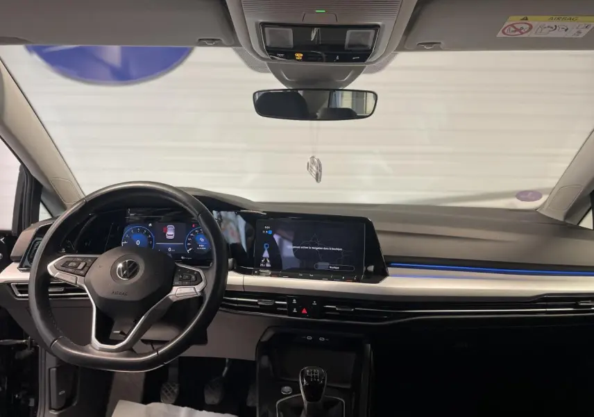 Intérieur noir de la Volkswagen Golf 1.5 eTSI 2024, vue frontale du tableau de bord avec volant et écran tactile.