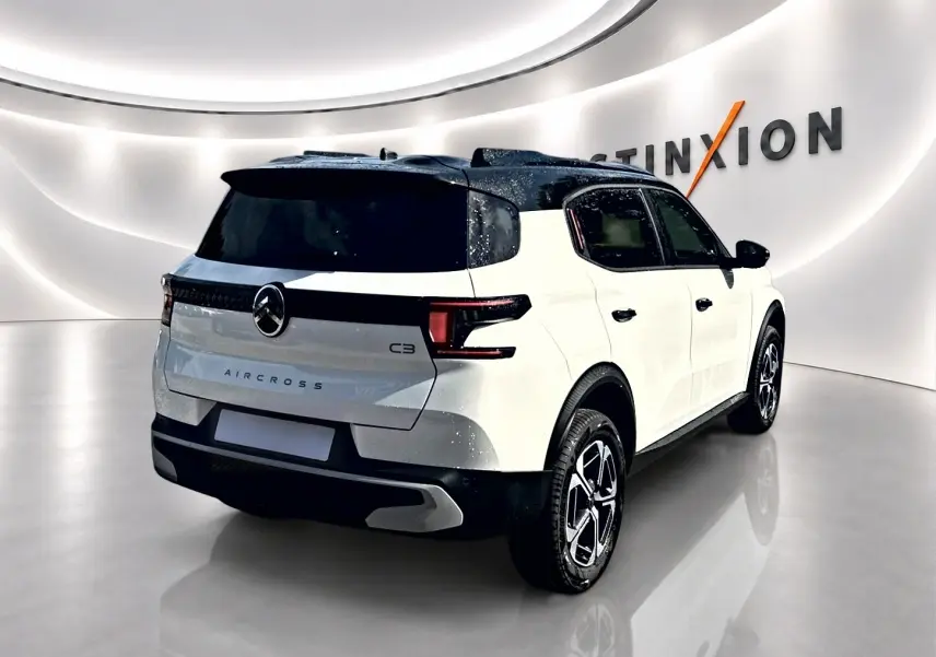 Vue 3/4 arrière droite d'un Citroën C3 Aircross blanc avec toit noir et jantes alu modernes dans un showroom.