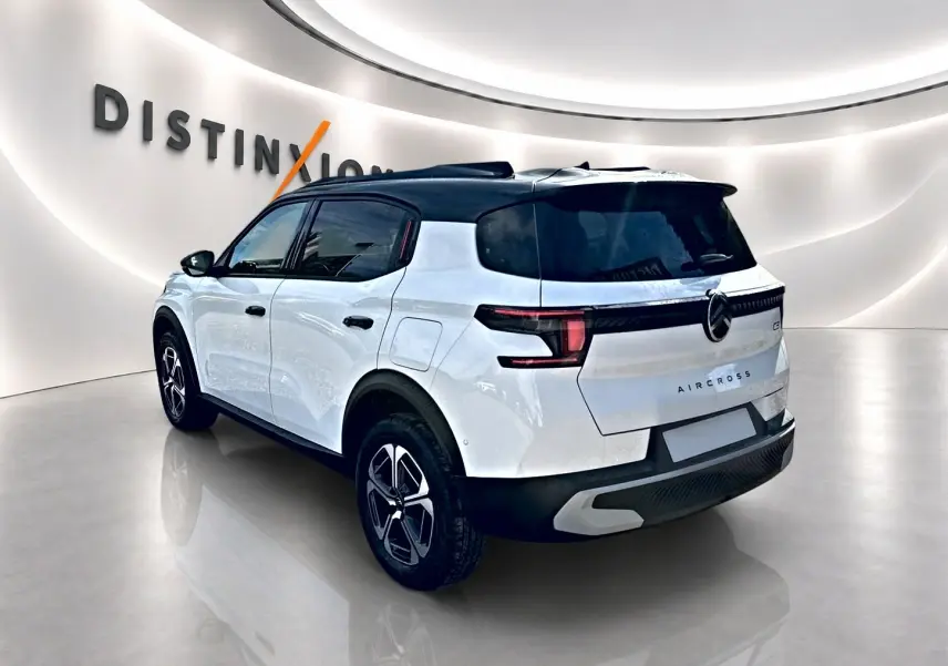 Vue 3/4 arrière droite d'un Citroën C3 Aircross blanc avec toit noir et jantes alu noires en showroom.
