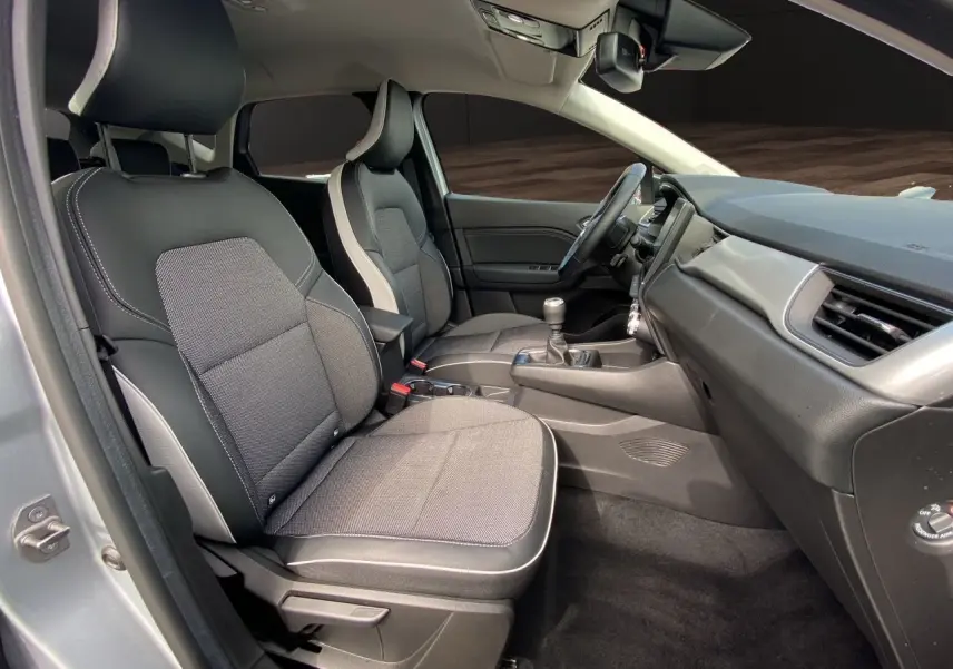 Vue intérieure côté conducteur du Renault Captur TCE 90 TECHNO 2024, sièges tissu noir avec surpiqûres grises et tableau de bord gris.