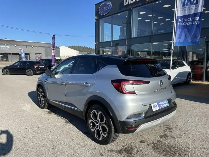 Vue 3/4 arrière droite d'un Renault Captur gris métal 2022 hybride avec toit noir et jantes distinctives.
