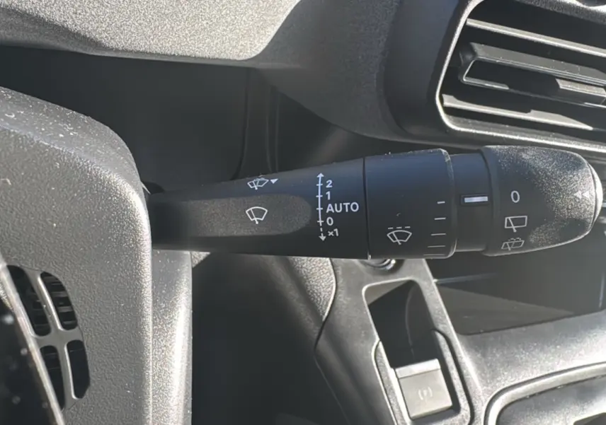 Gros plan sur la commande des essuie-glaces à gauche du volant dans l’habitacle du Peugeot Rifter noir Perla Nera 2025.