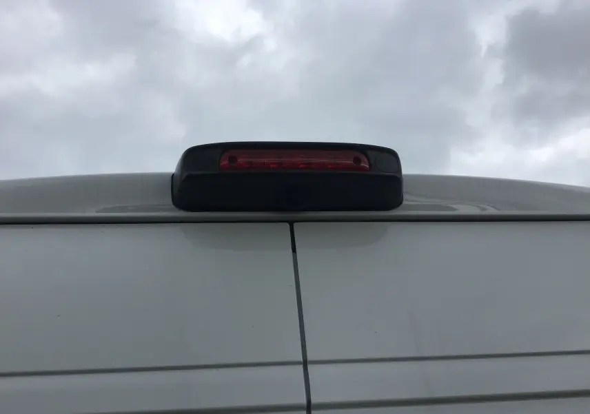 Gros plan sur l'arrière blanc du Peugeot Boxer Fourgon avec feu stop et caméra de recul intégrée sous un ciel nuageux.
