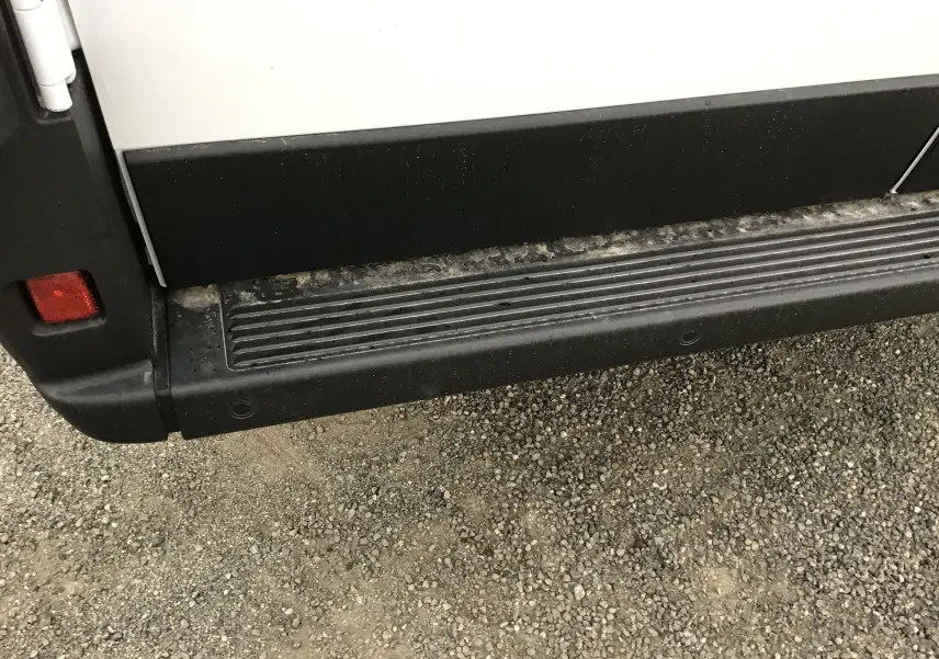 Gros plan sur la marche latérale noire du côté gauche d’un Peugeot Boxer Fourgon blanc, avec traces de boue.