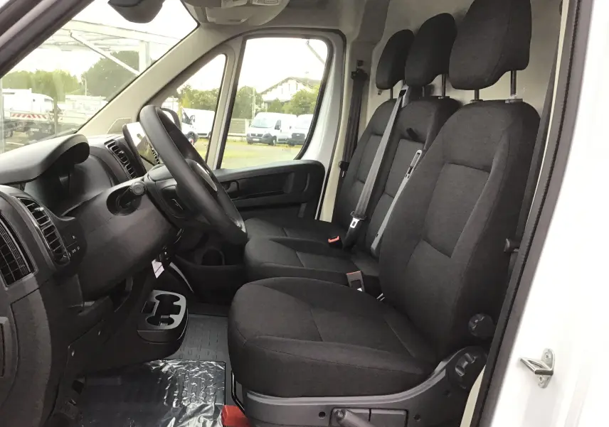 Vue intérieure côté conducteur du Peugeot Boxer Fourgon blanc 2025, montrant les sièges noirs et le tableau de bord.