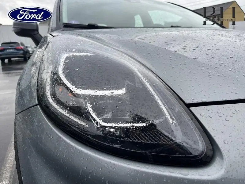 Gros plan sur le phare avant gauche d’un Ford Puma 2023 gris Solar métallisé avec gouttes de pluie visibles.