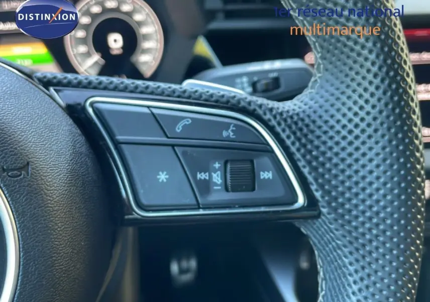 Gros plan sur les commandes gauche du volant en cuir perforé de l'Audi A3 Sportback noire 2025, affichage numérique en arrière-plan.