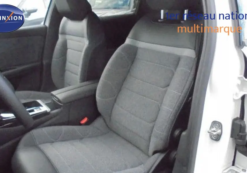 Intérieur du siège conducteur gris foncé d'une Citroën C5 X blanc métal, avec accoudoir et partie du tableau de bord visibles.