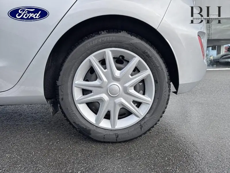 Gros plan sur la roue arrière droite d'une Ford Fiesta gris lunaire avec enjoliveur étoile sur fond de sol asphalté.