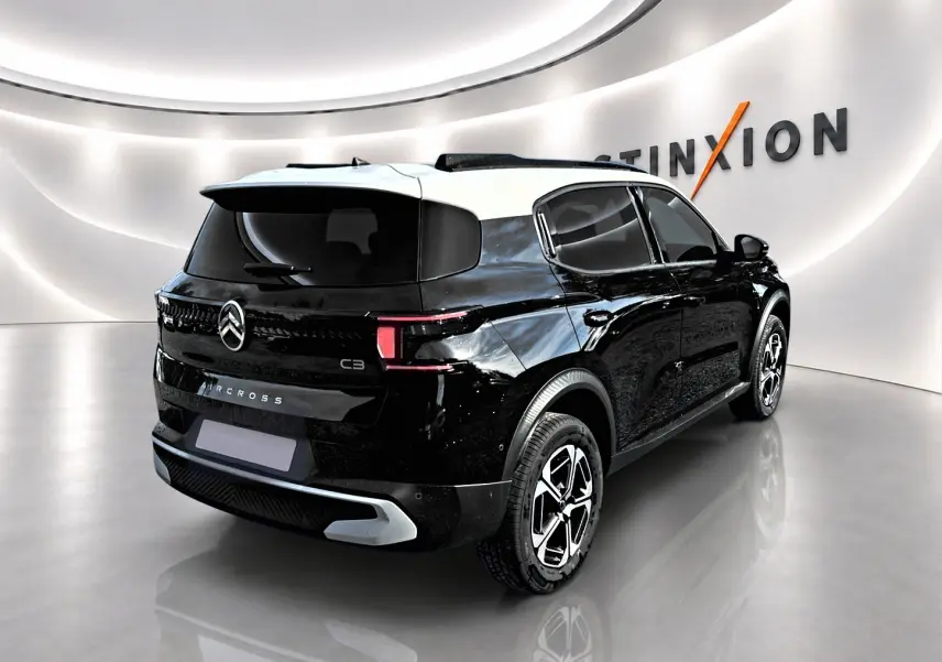 Vue 3/4 arrière droite d'une Citroën C3 Aircross noire avec toit blanc et jantes alu distinctives dans un showroom lumineux.