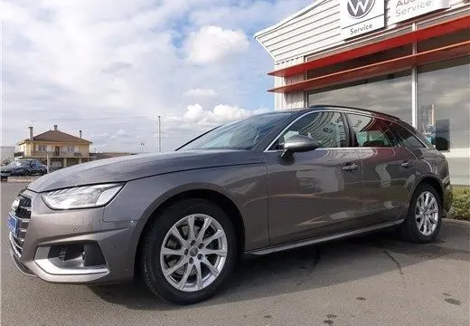Audi A4 Avant Business gris Terra vue 3/4 avant droit, stationnée devant un bâtiment de service Volkswagen.