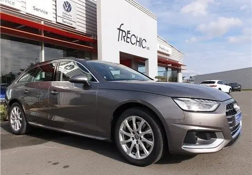 Audi A4 Avant Business gris Terra vue 3/4 avant droit, stationnée devant un garage Volkswagen avec jantes alliage visibles.