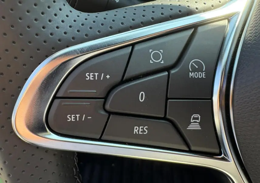 Gros plan sur les commandes de régulateur de vitesse au volant perforé du Renault Symbioz blanc nacré.