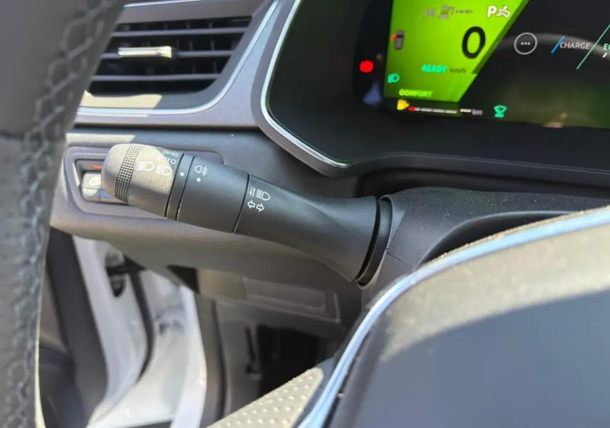 Gros plan sur la manette des feux et clignotants à gauche du volant d'une Renault Symbioz blanc nacré, tableau de bord numérique vert.