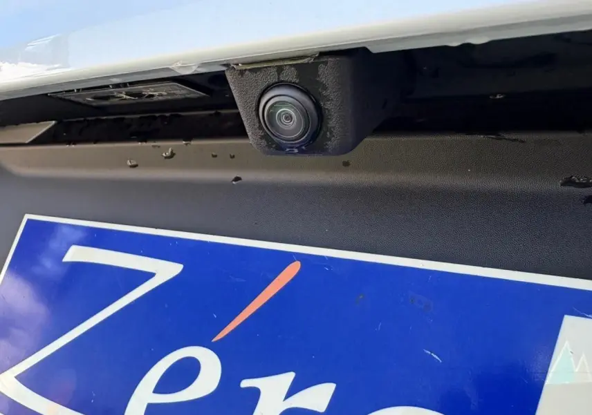 Gros plan sur la caméra de recul sous le pare-chocs arrière d'une Renault Symbioz blanc nacré.