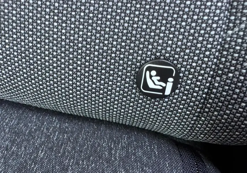 Gros plan sur le tissu gris du siège arrière avec l'icône du système Isofix visible sur la Renault Symbioz blanche nacrée.