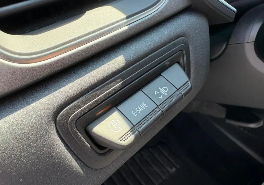 Gros plan sur les boutons de commande E-SAVE et réglage des phares dans l'habitacle noir du Renault Symbioz blanc nacré 2025.