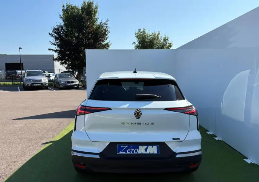 Vue arrière d'une Renault SYMBIOZ blanc nacré stationnée, avec feux arrière LED et logo central visible.