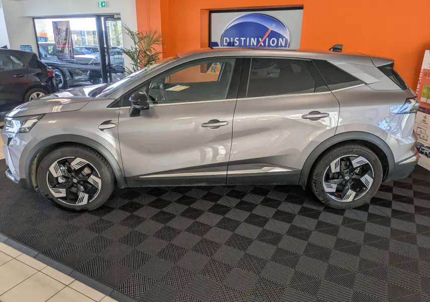 Vue 3/4 avant d'un Renault Symbioz gris cassiopée métal, avec calandre lumineuse et jantes bi-ton distinctives.