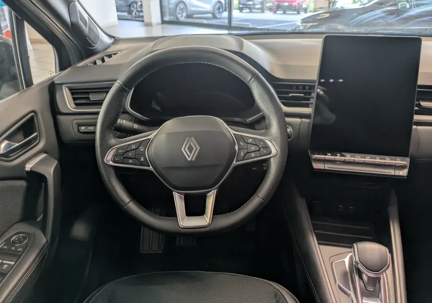 Vue intérieure centrée sur le volant noir Renault et l'écran tactile vertical du tableau de bord du Symbioz gris Cassiopée.
