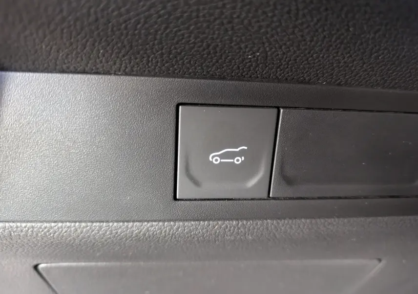 Bouton intérieur noir avec pictogramme blanc d'ouverture de coffre sur Renault Symbioz gris Cassiopée, vue rapprochée.