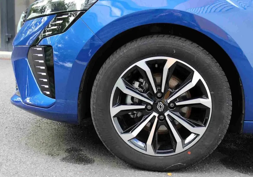 Gros plan sur la roue avant droite d'une Renault Clio bleu iron metal avec jante alliage noire et argentée.
