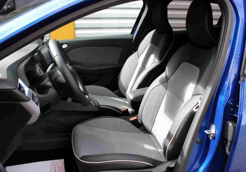 Vue intérieure côté conducteur de la Renault Clio bleu iron metal, volant multifonction et écran tactile central visible.