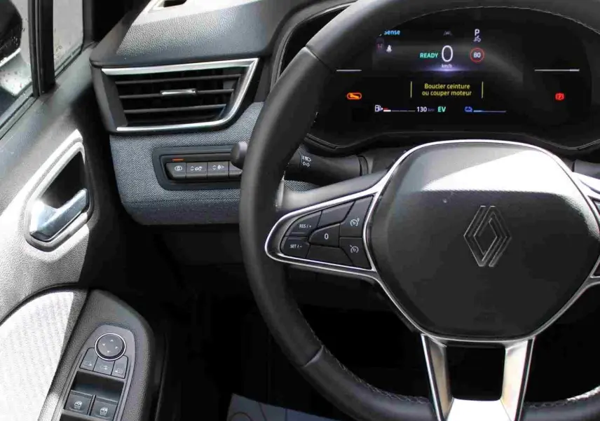 Vue intérieure centrée sur le volant noir de la Renault Clio 2025 avec tableau de bord numérique et commandes au volant.
