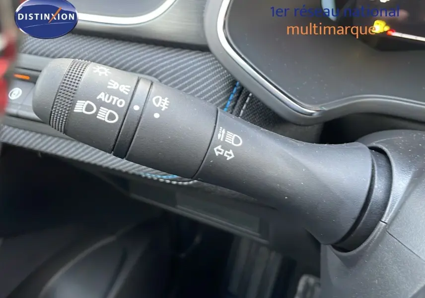 Gros plan sur la commande des phares et clignotants du Renault Captur E-Tech hybride 2025, intérieur noir et coutures bleues.